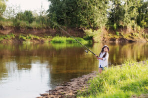 Joyeuse petite fille avec une canne à pêche au bord de l'étang en été